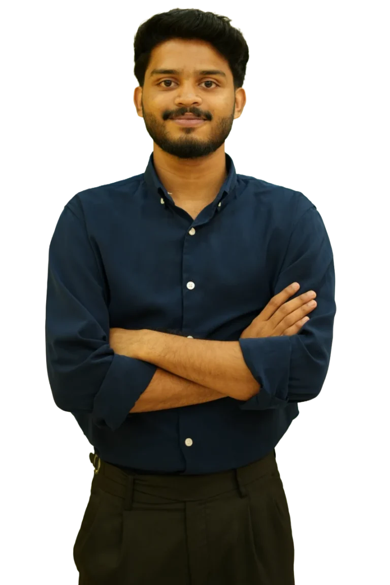 Young man with short black hair and a trimmed beard, wearing a dark blue shirt, standing with arms crossed and looking confidently at the camera against a plain background.